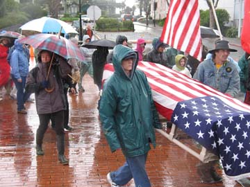 [Peace parade marchers with umbrellas in the rain, carrying flag-draped coffin]