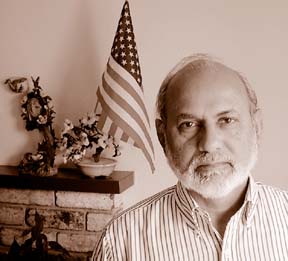 Abdul Aziz standing in front of mantle with American flag and floral arrangement